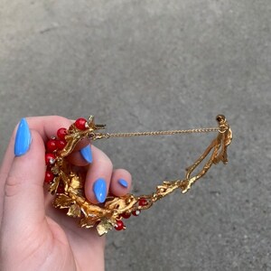 May include: Gold tone necklace with a red berry and leaf design. The necklace has a delicate chain and a clasp.