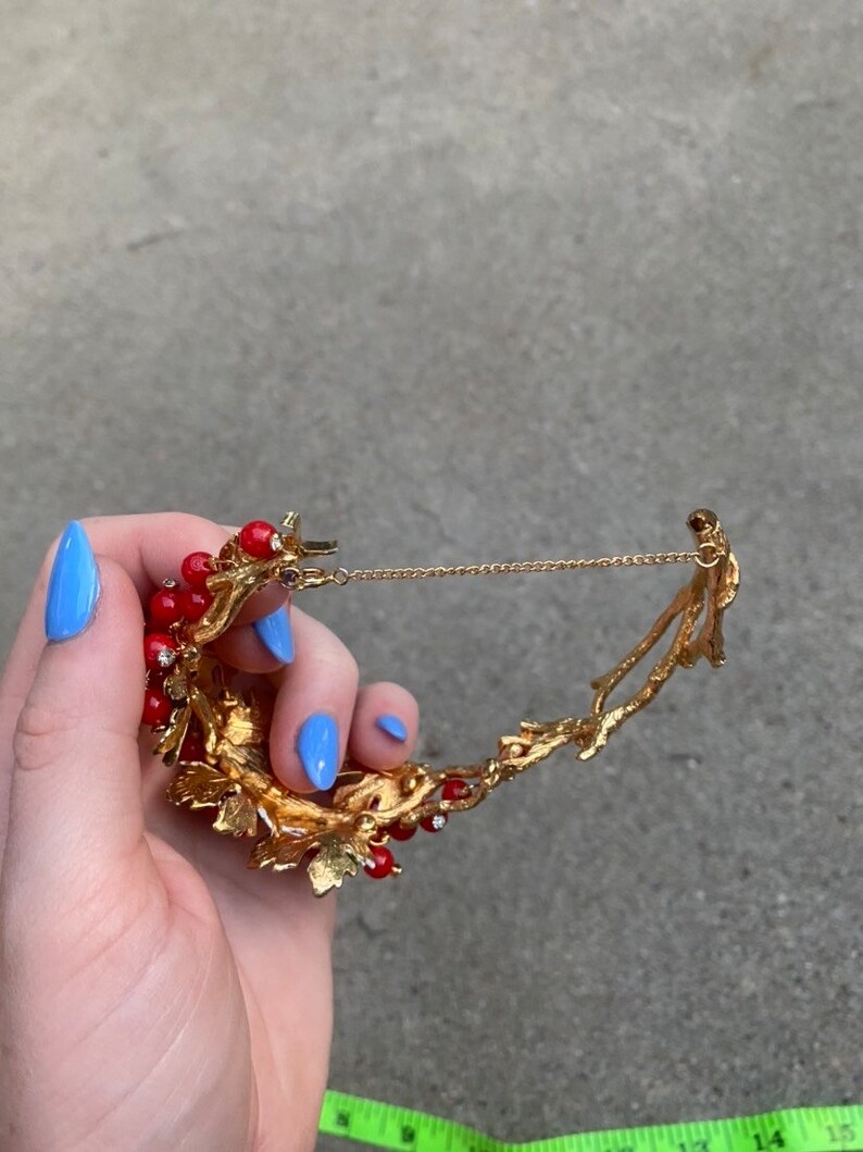 May include: Gold tone necklace with a red berry and leaf design. The necklace has a delicate chain and a clasp.