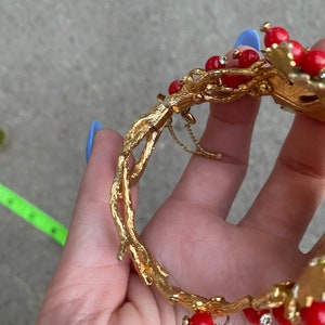 May include: Gold-tone bracelet with a branch design and red and clear stones. The bracelet has a hinged clasp.