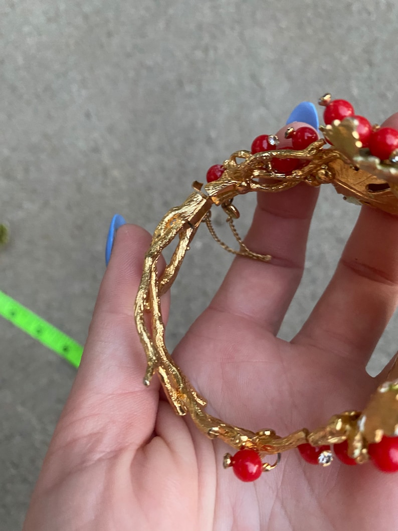May include: Gold-tone bracelet with a branch design and red and clear stones. The bracelet has a hinged clasp.