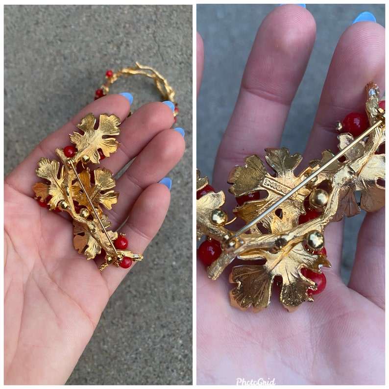 May include: Gold-toned brooch with red glass beads and a leaf design. The brooch has a pin back and is marked "Boucher" on the back.