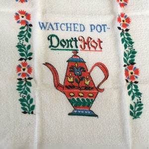 Może przedstawiać: Biały ręcznik kuchenny z zielono-czerwonym kwiatowym obramowaniem. W środku ręcznika znajduje się czerwony czajnik z zielonym, niebieskim i żółtym wzorem kwiatowym. Na ręczniku nadrukowany jest tekst "WATCHED POT-Don't Hot".