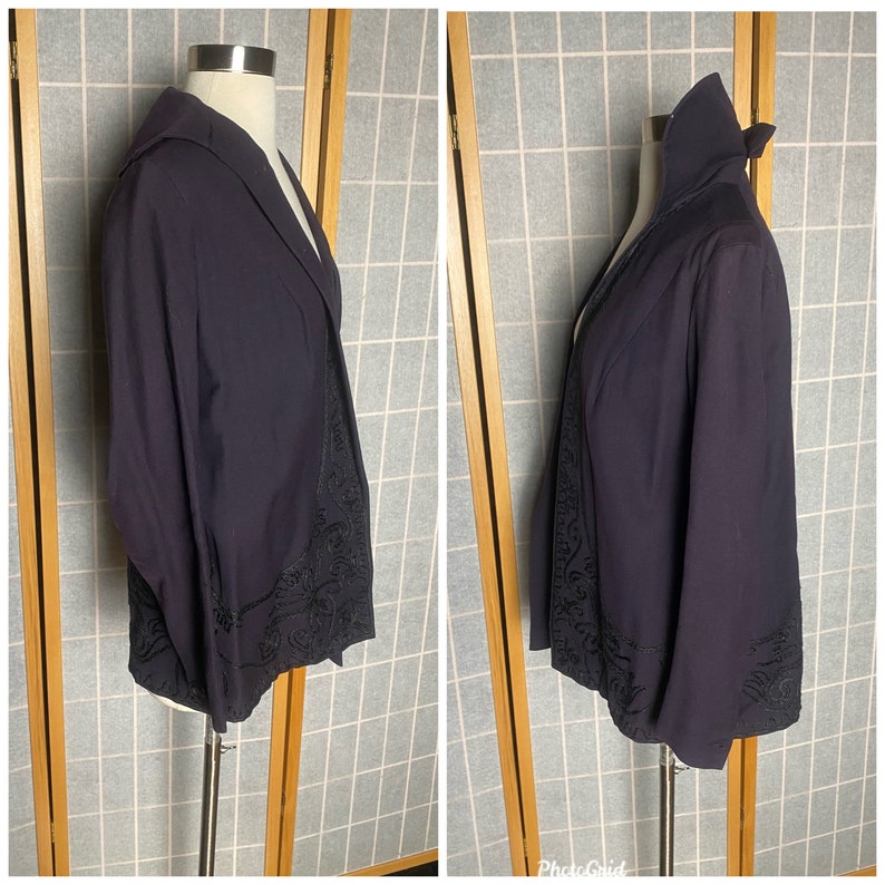 Puede incluir: Una chaqueta azul marino oscuro con cuello alto y mangas largas. La chaqueta tiene un dise&ntilde;o bordado negro decorativo alrededor del dobladillo y los pu&ntilde;os.