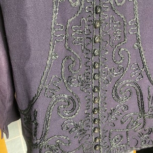 Puede incluir: Una chaqueta de color morado oscuro con detalles bordados en negro y una fila de botones negros en la espalda.