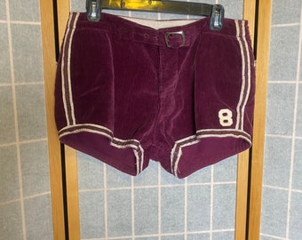 May include: Burgundy corduroy shorts with white piping and a white number "8" on the right leg. The shorts have a belt loop and a belt.
