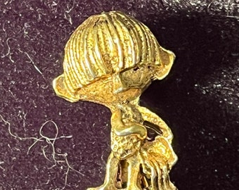 Vintage 1970s gold tone pin of a mop top child with a bowl cut holding a peanut.