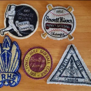 Può includere: Una collezione di toppe da baseball vintage. Una toppa presenta un giocatore di baseball e il testo "1953 Powell River Baseball Champions". Un'altra toppa è una palla da baseball con "1952 Powell River Midget Baseball Champs". Altre toppe includono "PRHS" e "Powell River Canada".