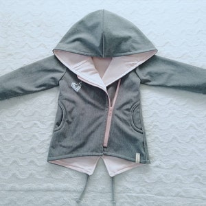 Könnte beinhalten: Eine graue Kapuzenjacke mit rosa Futter und Reißverschluss. Die Jacke hat ein kleines herzförmiges Design auf der Vorderseite.