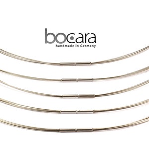 May include: A collection of silver-toned wire necklaces with a minimalist design. Each necklace is composed of multiple strands of thin wire, connected by small, cylindrical clasps. The brand name "bocara handmade in Germany" is visible.