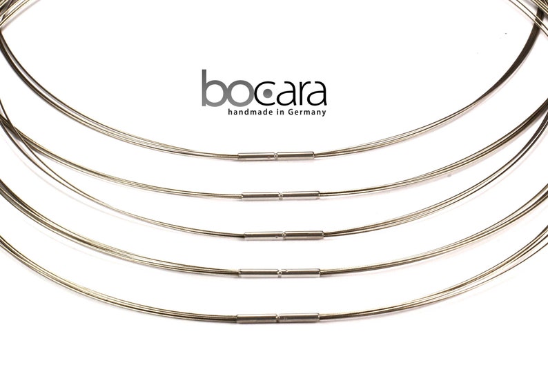 May include: A collection of silver-toned wire necklaces with a minimalist design. Each necklace is composed of multiple strands of thin wire, connected by small, cylindrical clasps. The brand name "bocara handmade in Germany" is visible.