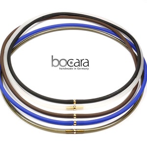 Könnte beinhalten: Eine Auswahl an Bocara-Halsketten in Schwarz, Weiß, Braun und Blau. Jede Halskette hat einen goldfarbenen Verschluss und wird in Deutschland handgefertigt.