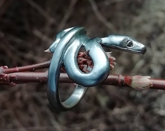 May include: A silver snake ring with a detailed, realistic design. The snake is coiled and has a raised head with a small, black eye.