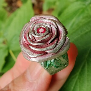 May include: A silver and pink rose ring with a red gemstone in the centre. The ring is made of polymer clay and is a unique piece of jewellery.