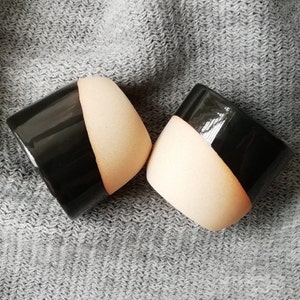 May include: Two ceramic planters, each with a black and beige color scheme. The planters are half black and half beige, with a smooth, rounded shape.