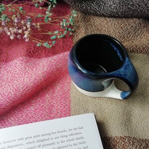 May include: A blue and white ceramic mug with a unique handle. The mug is sitting on a plaid blanket with dried flowers.