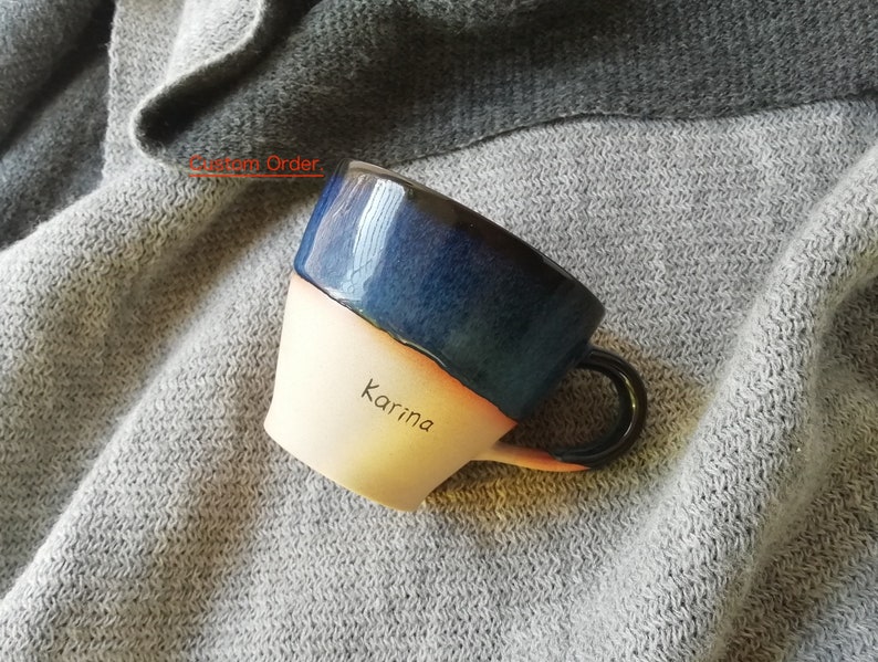 May include: A ceramic mug with a blue and white glaze. The mug has a handle and the name "Karina" is written on the side.