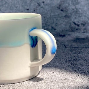 May include: White ceramic mug with a blue and white glaze design. The mug has a rounded handle.