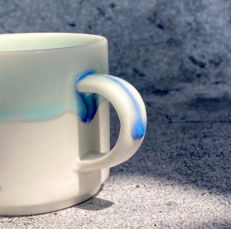 May include: White ceramic mug with a blue and white glaze design. The mug has a rounded handle.