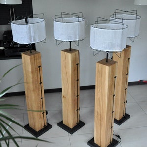 Op de afbeelding: Vier houten vloerlampen met witte stoffen lampenkappen en zwarte metalen frames. De lampen staan op een betegelde vloer. De lampen zijn gemaakt van natuurlijk hout en hebben een rustieke uitstraling.