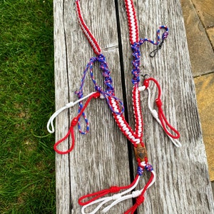 May include: A red, white, and blue paracord lanyard with a wooden bead and multiple loops. The lanyard is made with a braided design.