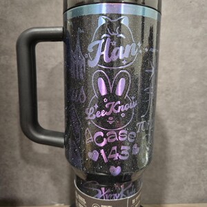May include: A black glitter travel mug with a handle, a black lid, and a straw. The mug features purple text and a bunny design that reads "Han", "Bee Know", and "A Case 145". The mug is designed for car cup holders.