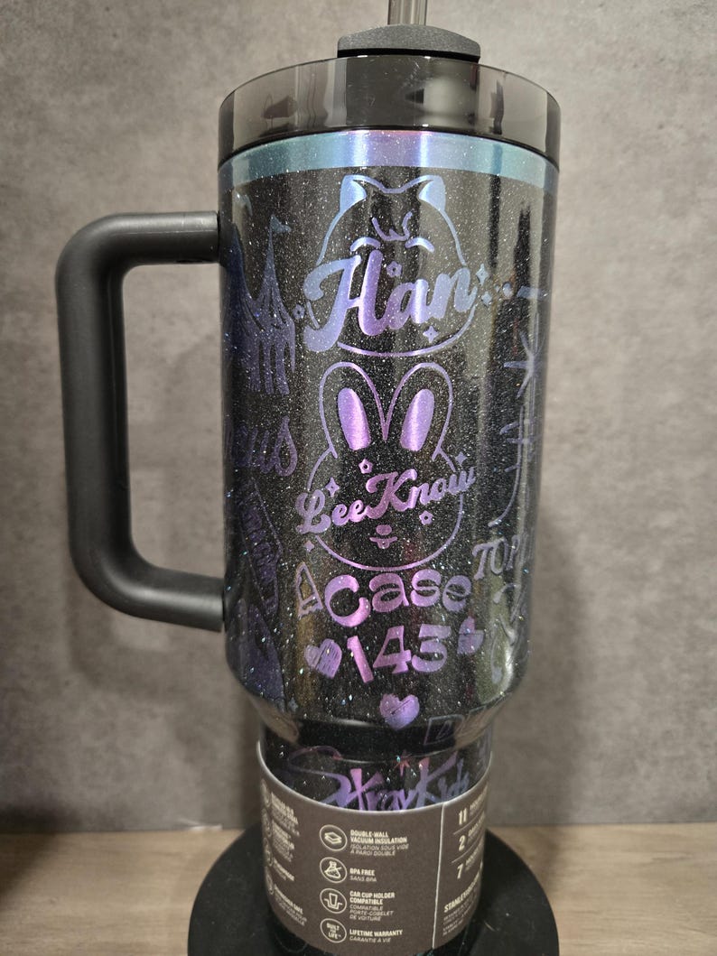 May include: A black glitter travel mug with a handle, a black lid, and a straw. The mug features purple text and a bunny design that reads "Han", "Bee Know", and "A Case 145". The mug is designed for car cup holders.