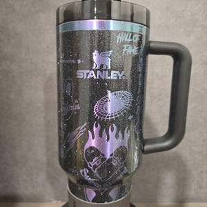 May include: Black Stanley Quencher Tumbler with a handle, featuring a glittery finish and various graphics. The tumbler has a black lid and handle, with the text "HALL OF FAME" and "STANLEY" visible. The tumbler holds 1.18L.