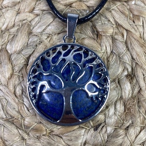 Peut inclure: Un pendentif en argent en forme d'arbre de vie avec une pierre de lapis-lazuli bleue. Le pendentif est sur un cordon noir.