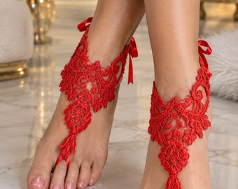 May include: A pair of bright red lace barefoot sandals featuring intricate floral embroidery patterns. Each sandal wraps around the ankle with a thin satin ribbon tie and includes a delicate loop that secures around the second toe for a secure fit.