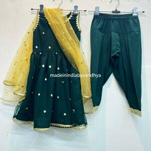 Puede incluir: Un conjunto verde y dorado para un ni&ntilde;o, que consta de un vestido sin mangas con un dupatta de red dorada y pantalones a juego. El vestido tiene lentejuelas doradas y un ribete dorado. El texto "madeinindiabysandhya" es visible en el vestido.