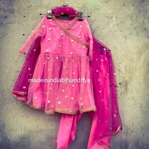 Puede incluir: Un conjunto de ni&ntilde;a rosa y dorado con una blusa de manga larga, una falda y una dupatta a juego. El conjunto est&aacute; decorado con peque&ntilde;as lentejuelas redondas de espejo. El texto "madeinindia bysandhya" es visible en la falda.