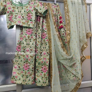May include: A mint green embroidered lehenga with a matching choli and a sheer dupatta. The lehenga and choli feature floral embroidery with pink and green accents. The dupatta has a gold border and is made of a sheer fabric.