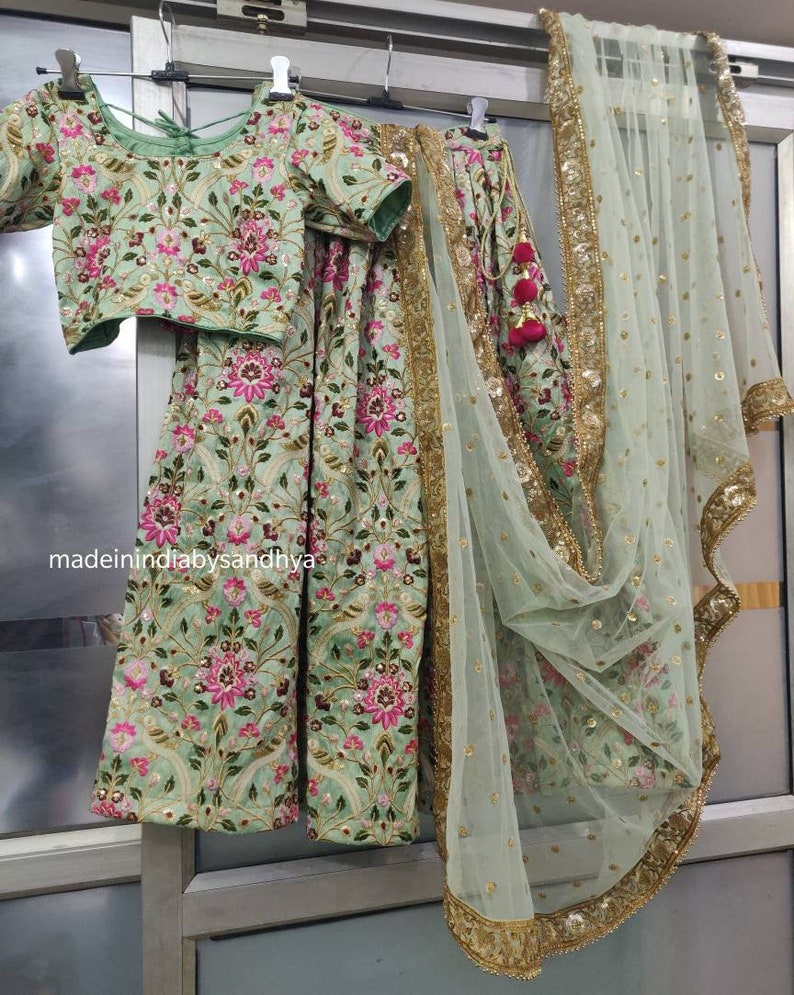 May include: A mint green embroidered lehenga with a matching choli and a sheer dupatta. The lehenga and choli feature floral embroidery with pink and green accents. The dupatta has a gold border and is made of a sheer fabric.