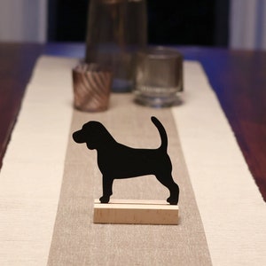 Könnte beinhalten: Schwarze Silhouette eines Hundes auf einem Holzsockel, der auf einem beigefarbenen Tischläufer mit einem braunen Holztisch im Hintergrund steht.