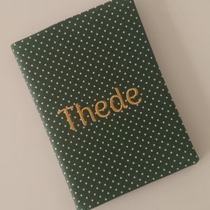 May include: A green notebook with white polka dots and the name "Thede" embroidered in gold thread.