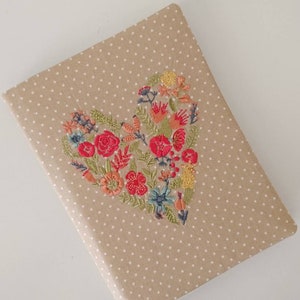 Peut inclure: Un carnet brun à pois blancs avec un motif de cœur brodé de fleurs colorées.