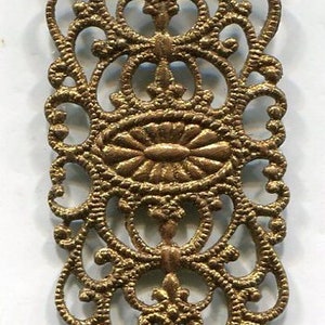 May include: Gold metal filigree embellishment with a decorative, ornate design. The filigree is rectangular in shape and has a detailed, intricate pattern.