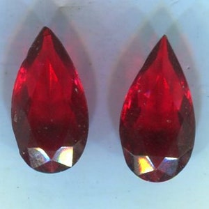 May include: Two teardrop-shaped red glass beads with a faceted design.