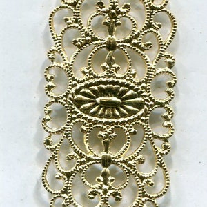 May include: Gold filigree metal embellishment with a delicate, intricate design. The embellishment is rectangular in shape and features a central oval with a radiating pattern.