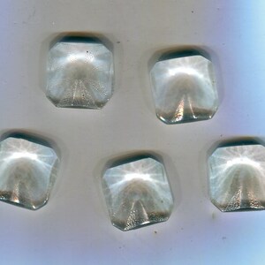 Op de afbeelding: Zes transparante glazen knopen met een stervormig patroon. De knopen zijn vierkant met afgeronde hoeken.