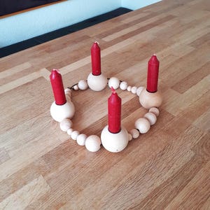 Puede incluir: Un portavelas de madera con cuatro velas rojas. El portavelas est&aacute; hecho de un c&iacute;rculo de cuentas de madera con cuatro portavelas unidos al c&iacute;rculo.