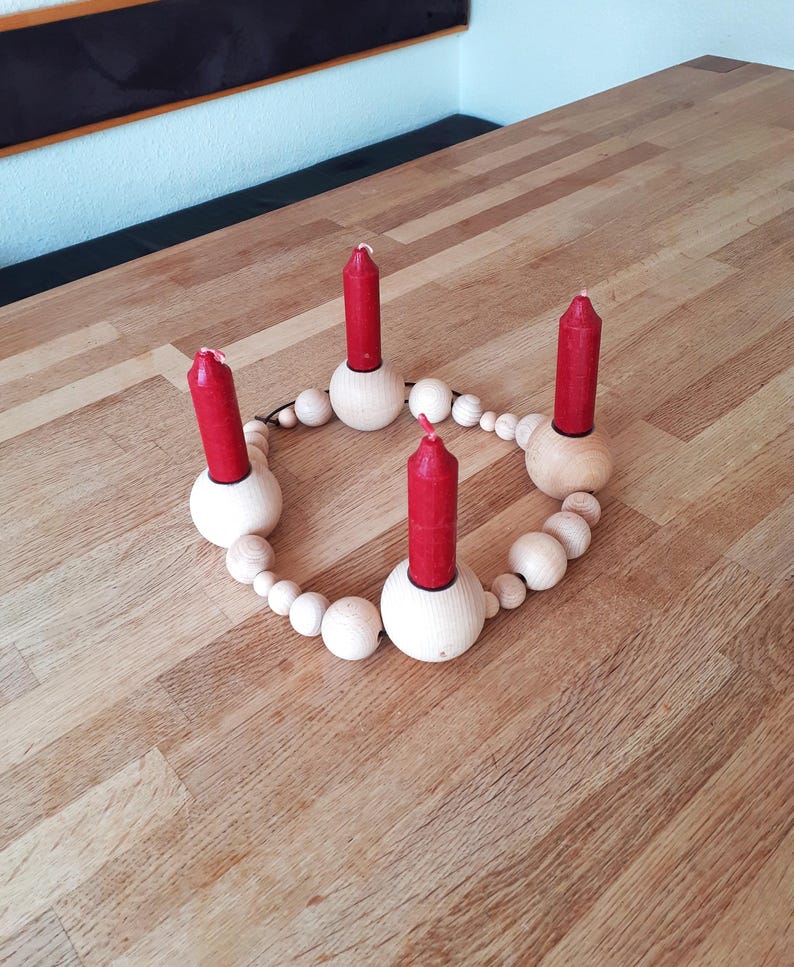Puede incluir: Un portavelas de madera con cuatro velas rojas. El portavelas est&aacute; hecho de un c&iacute;rculo de cuentas de madera con cuatro portavelas unidos al c&iacute;rculo.