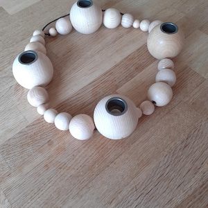 Puede incluir: Un portavelas de madera con un dise&ntilde;o circular. El portavelas est&aacute; hecho de cuentas de madera natural y tiene cinco vasos para velas. Los vasos para velas son de metal y tienen un acabado gris oscuro.