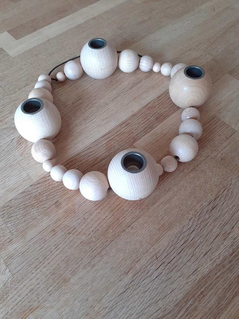 Puede incluir: Un portavelas de madera con un dise&ntilde;o circular. El portavelas est&aacute; hecho de cuentas de madera natural y tiene cinco vasos para velas. Los vasos para velas son de metal y tienen un acabado gris oscuro.
