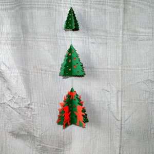 Könnte beinhalten: Drei Papier-Weihnachtsbäume hängen an einer Schnur. Der obere Baum ist grün, der mittlere Baum ist grün mit roten Akzenten und der untere Baum ist grün mit roten Figuren.