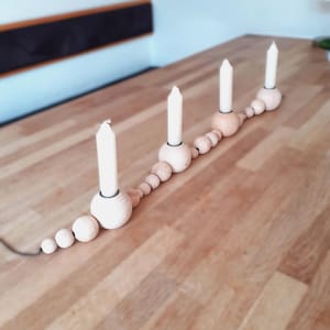 Puede incluir: Un portavelas de madera con una cadena de cuentas de madera. El portavelas tiene cuatro velas blancas.