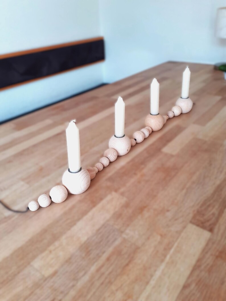 Puede incluir: Un portavelas de madera con una cadena de cuentas de madera. El portavelas tiene cuatro velas blancas.