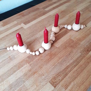 Puede incluir: Un portavelas de madera con una cadena de cuentas de madera. Cuatro velas rojas se colocan en el portavelas.