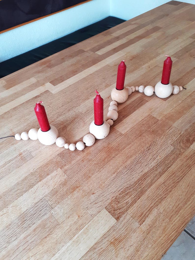 Puede incluir: Un portavelas de madera con una cadena de cuentas de madera. Cuatro velas rojas se colocan en el portavelas.