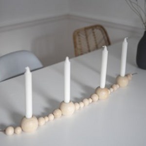 Puede incluir: Un portavelas de madera con un dise&ntilde;o de cuentas y cuatro velas blancas. El portavelas est&aacute; sobre una mesa blanca.